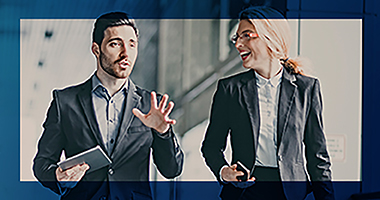 Caucasian business man in a suit holding a tablet while talking to a Caucasian business woman in a suit