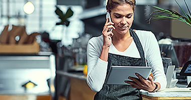 Female restaurant employee talking on a mobile phone while looking at a tablet.